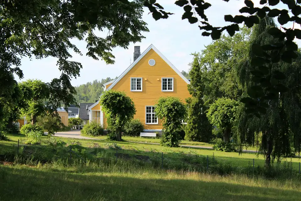 Gult trehus med hvite vinduer omgitt av trær og plen