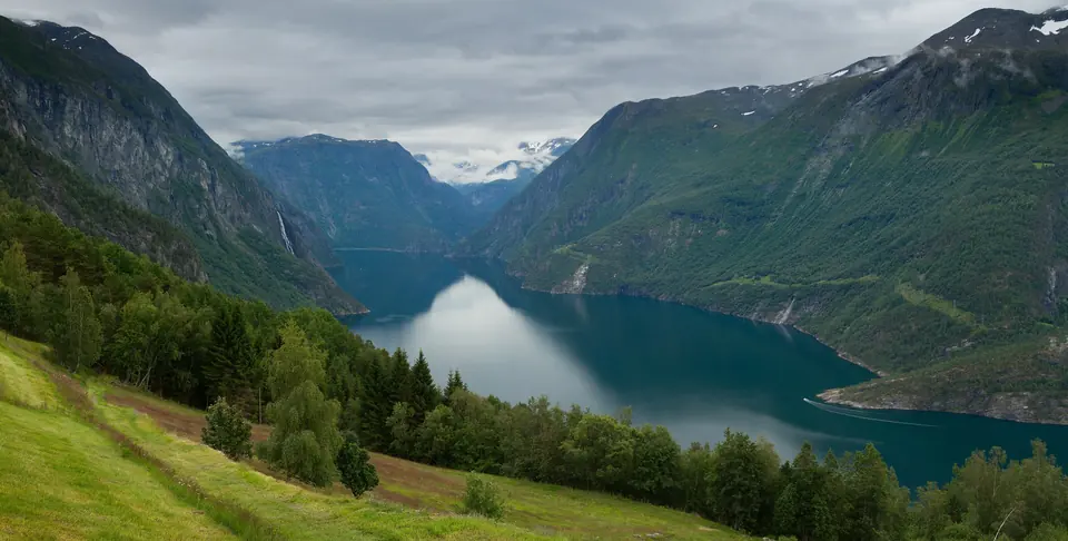 Utsikt over Tafjorden på Sunnmøre med grønne fjellsider, skog og snø på toppene
