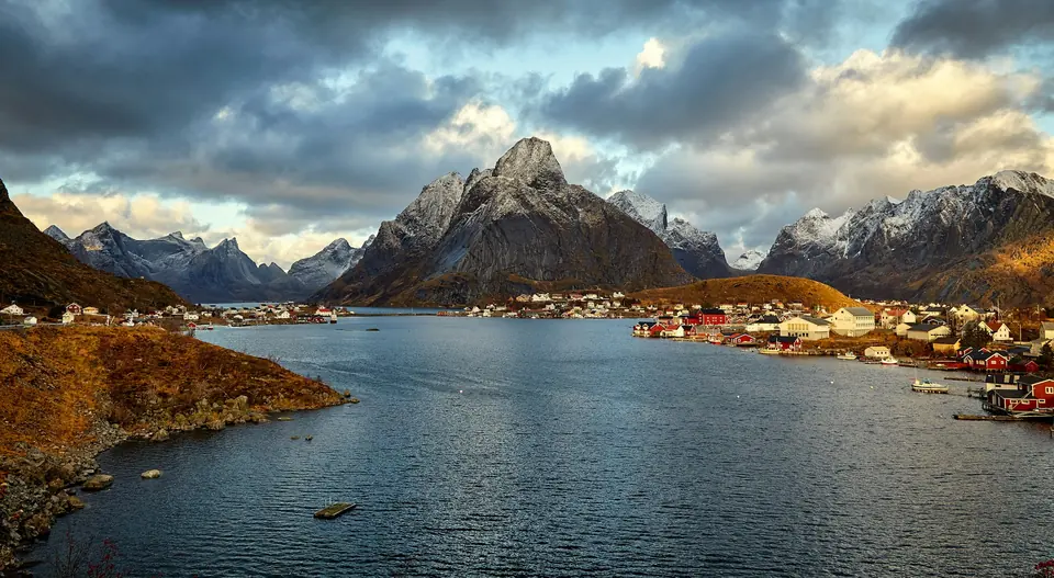 Fiskevær med røde rorbuer ved en fjord under spisse fjelltopper