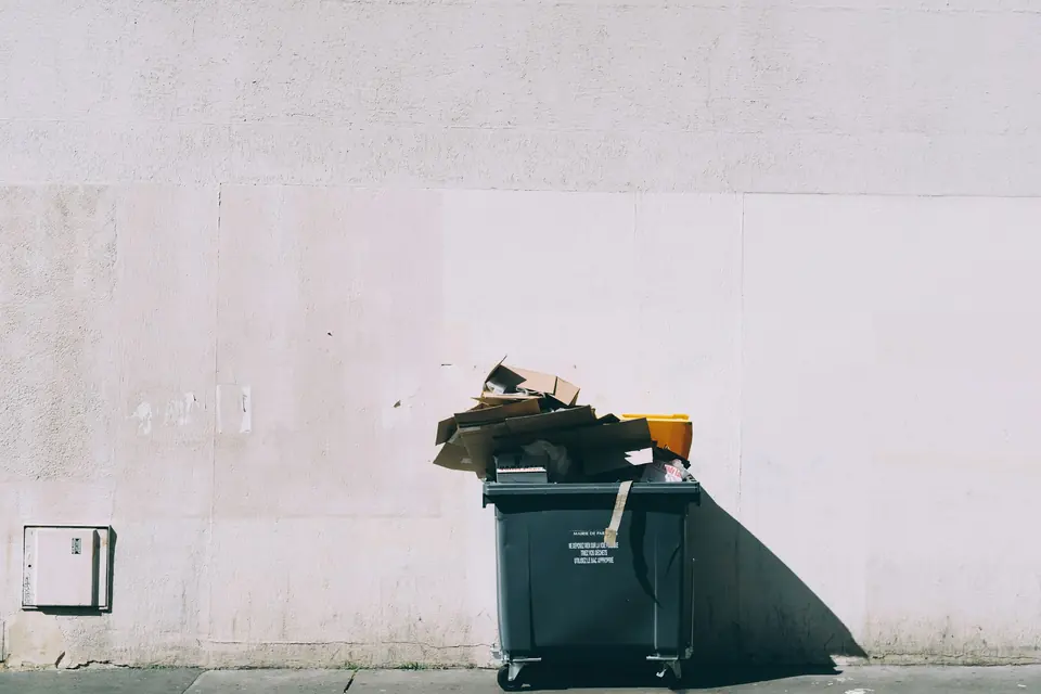 Overfull avfallscontainer med pappesker inntil en lys murvegg