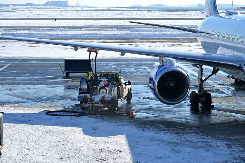 Tankvogn fyller drivstoff under vingen på et passasjerfly på en snødekt flyplass